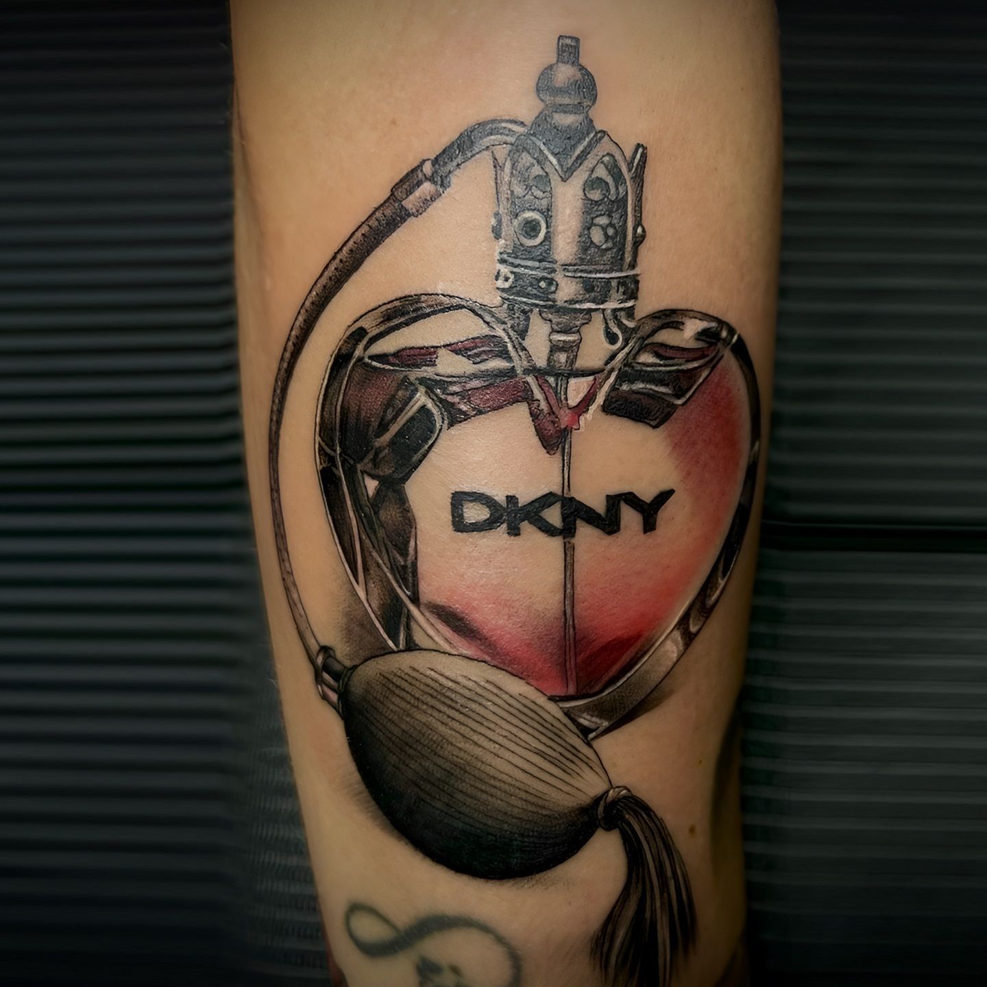 Tatuaje en color de un frasco de perfume DKNY realizado por Aitor Murga en Ink for All